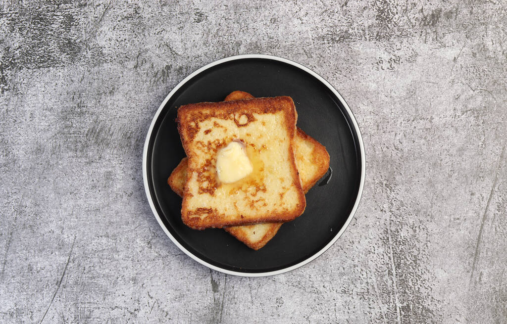 French toast with melting butter on a round plate on a dark gray background. Top view, flat lay - Photo, Image