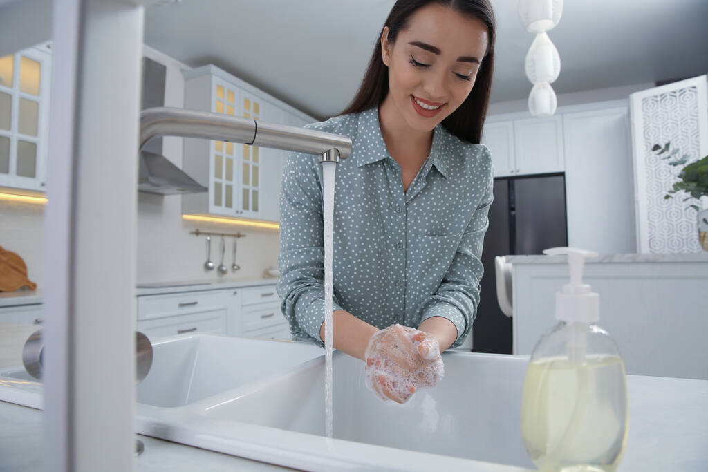 Jeune femme se lave les mains avec du savon liquide dans la cuisine - Photo, image