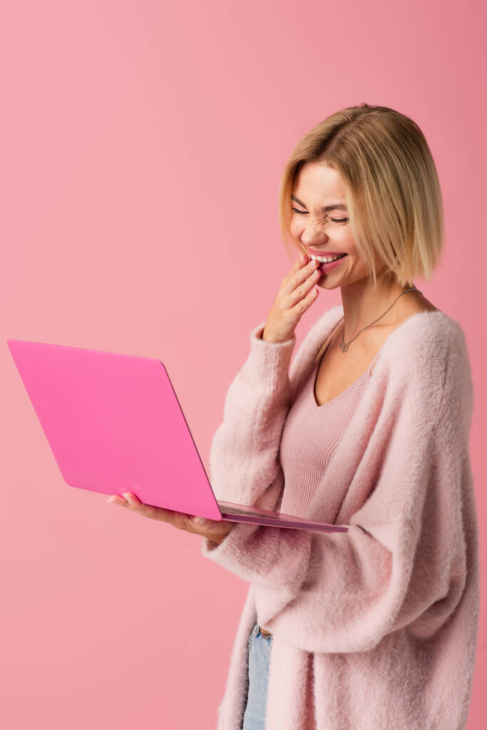 onnellinen nuori nainen käyttää kannettavaa tietokonetta ja nauraa eristetty vaaleanpunainen  - Valokuva, kuva