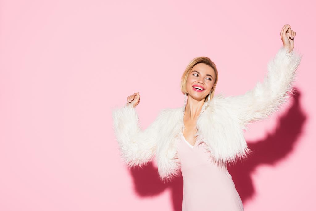 aufgeregte blonde Frau in Slip-Kleid und Kunstpelzjacke auf rosa  - Foto, Bild