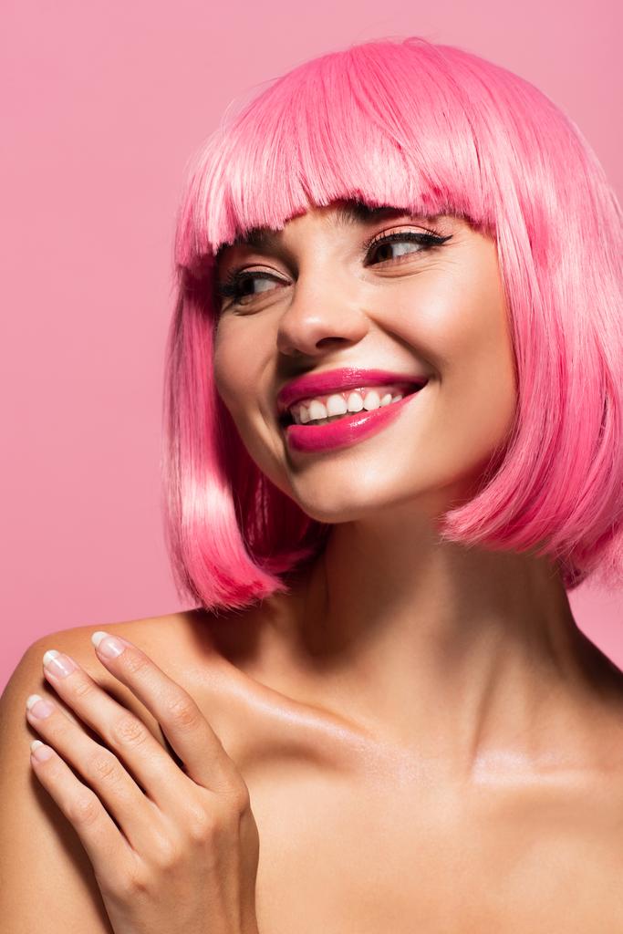 Ευτυχισμένη νεαρή γυναίκα με χρωματιστά μαλλιά κοιτάζει μακριά απομονωμένη σε ροζ  - Φωτογραφία, εικόνα