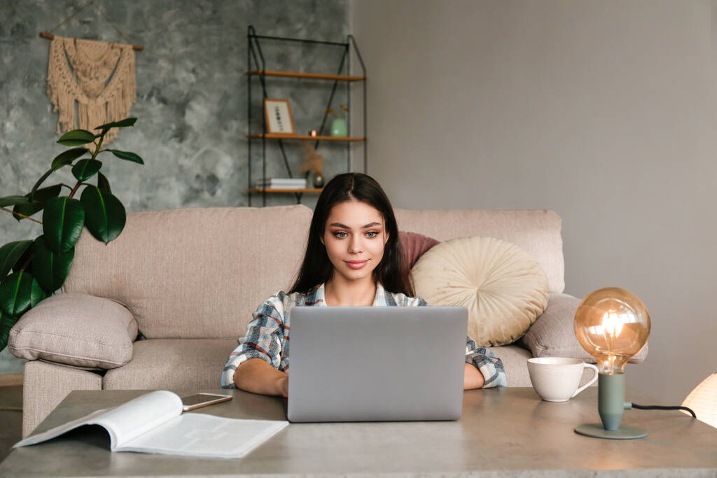 Online-Bildungskonzept. Junge schöne brünette Frau tippt auf ihrem Laptop. Porträt einer College-Studentin, die zu Hause studiert. Nahaufnahme, Kopierraum, Hintergrund. - Foto, Bild