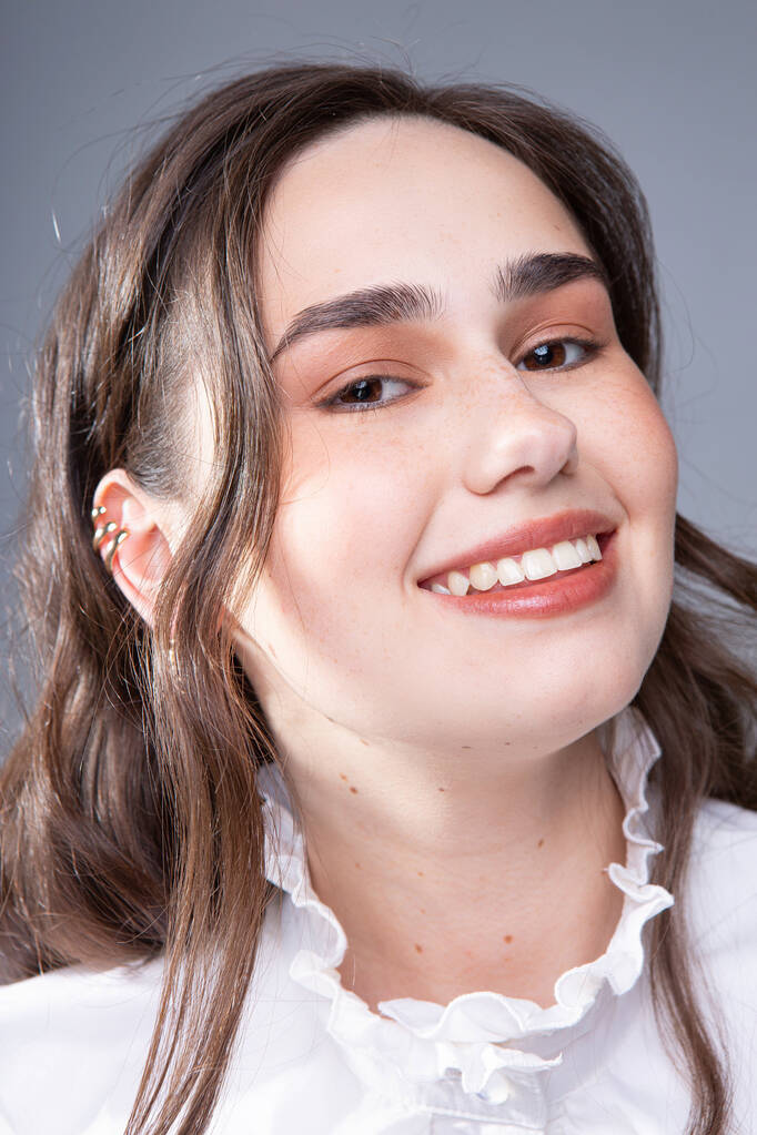 Retrato de una joven sonriente de pelo largo con ojos marrones oscuros aislados en gris - Foto, imagen