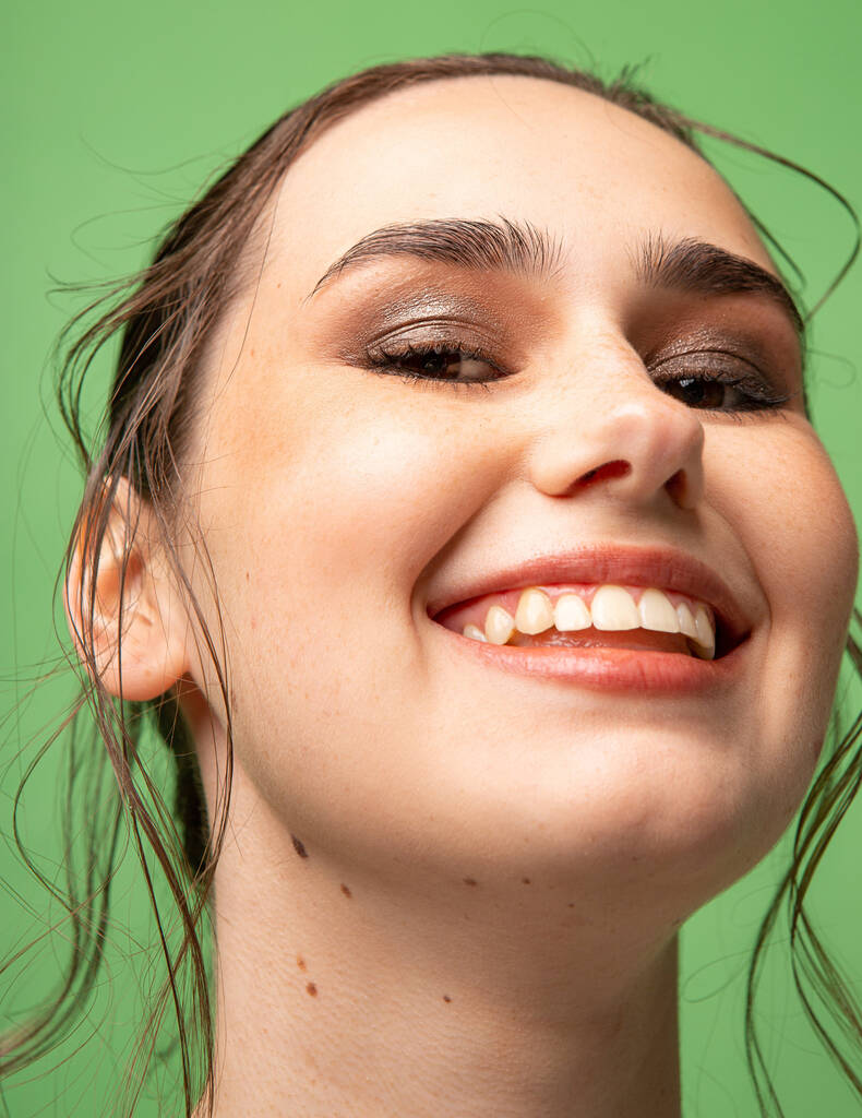 Detailní portrét usmívající se mladé ženy se sebranými tmavými vlasy s hnědýma očima izolované na zelené - Fotografie, Obrázek