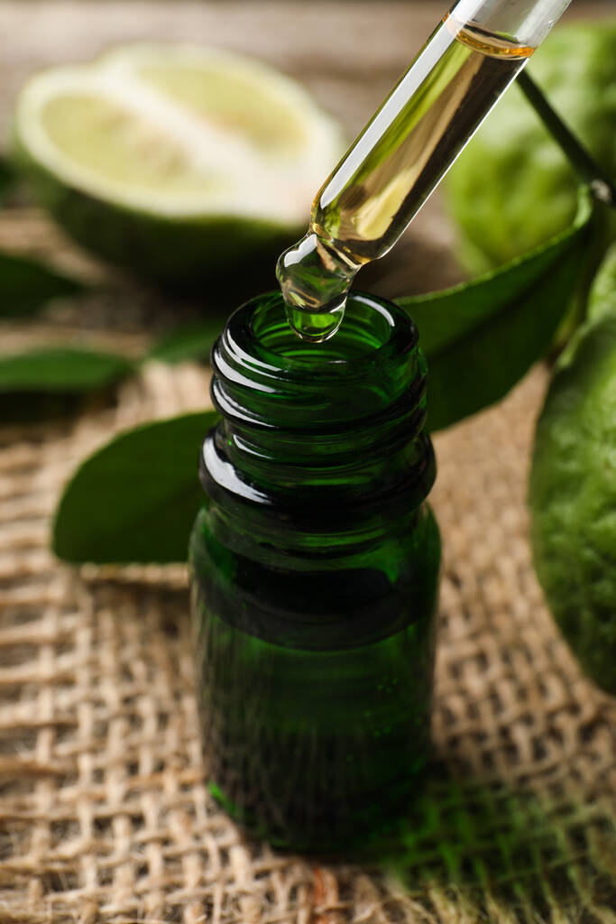 Aceite esencial de bergamota goteando de la pipeta en botella sobre la mesa, primer plano - Foto, imagen