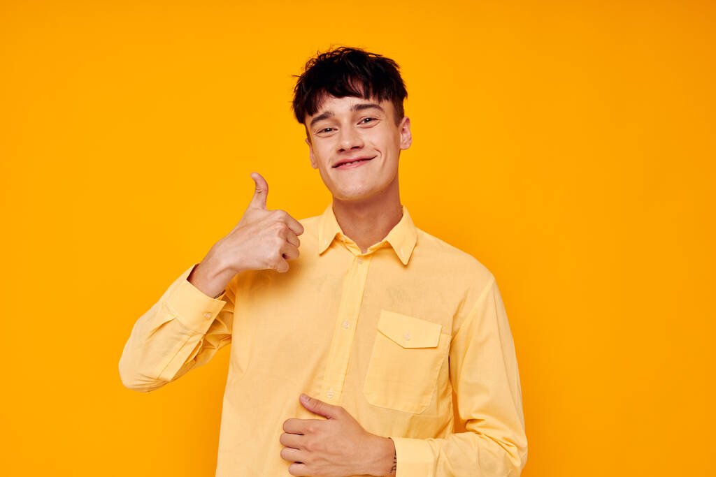 Χαρούμενος νεαρός με κίτρινη μπλούζα και χειρονομίες με τα χέρια του. - Φωτογραφία, εικόνα