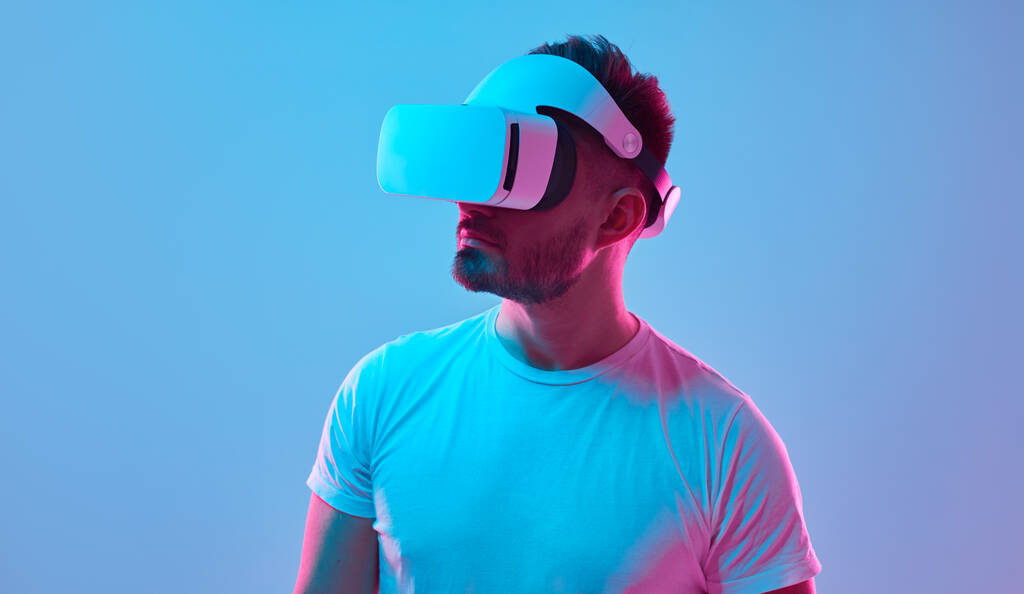 VR kulaklıklı adam stüdyoda neon ışıklarıyla sanal gerçeklik yaşıyor. - Fotoğraf, Görsel
