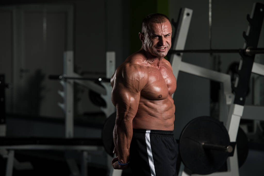 Magnifique sportif mâle puissance, homme musclé dans la salle de gym haltère flexion muscles-modèle de remise en forme debout fort et le menton - Photo, image