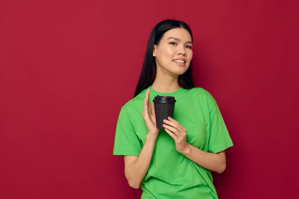 Nainen, jolla on aasialainen ulkonäkö vihreässä t-paidassa lasillinen juomaa hauskaa eristetty tausta muuttamaton - Valokuva, kuva