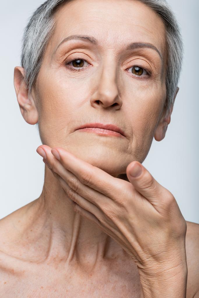 donna di mezza età toccando mento isolato su grigio - Foto, immagini