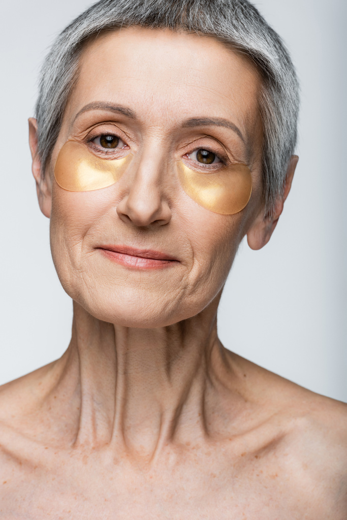 задоволена жінка середнього віку в золотих окулярах, дивлячись на камеру ізольовано на сірому
 - Фото, зображення