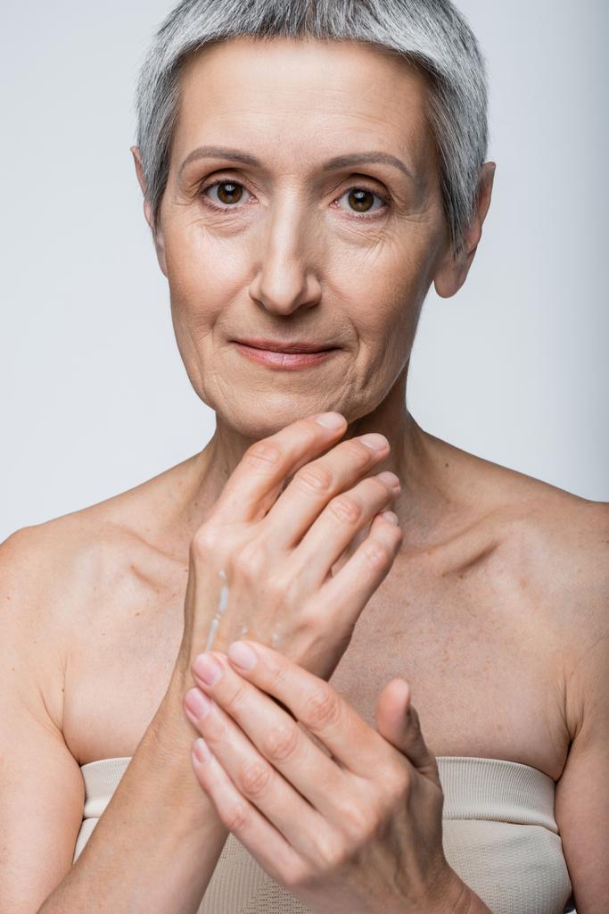 middle aged woman applying cream on hand isolated on grey  - Photo, Image