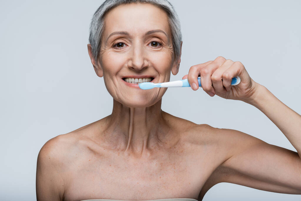 allegra donna di mezza età che tiene lo spazzolino da denti e lavarsi i denti isolati su grigio  - Foto, immagini