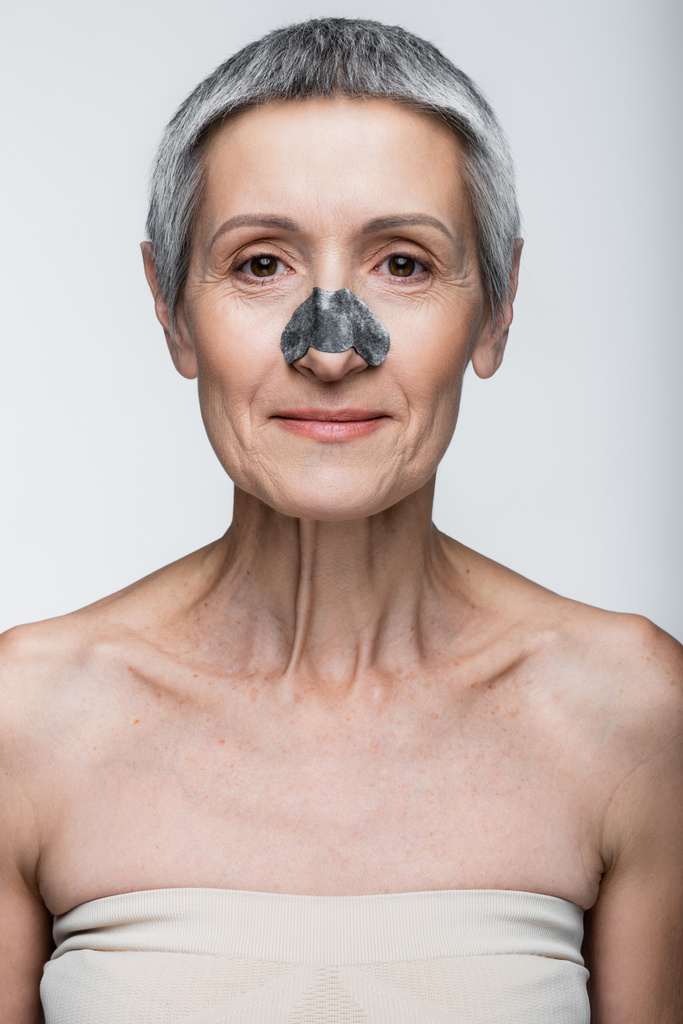 glimlachende volwassen vrouw met zwarte vlek op neus geïsoleerd op grijs  - Foto, afbeelding