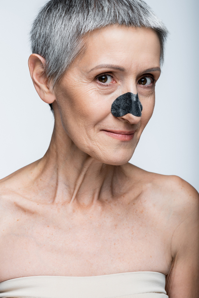alegre mujer de mediana edad con parche negro en la nariz aislado en gris  - Foto, Imagen