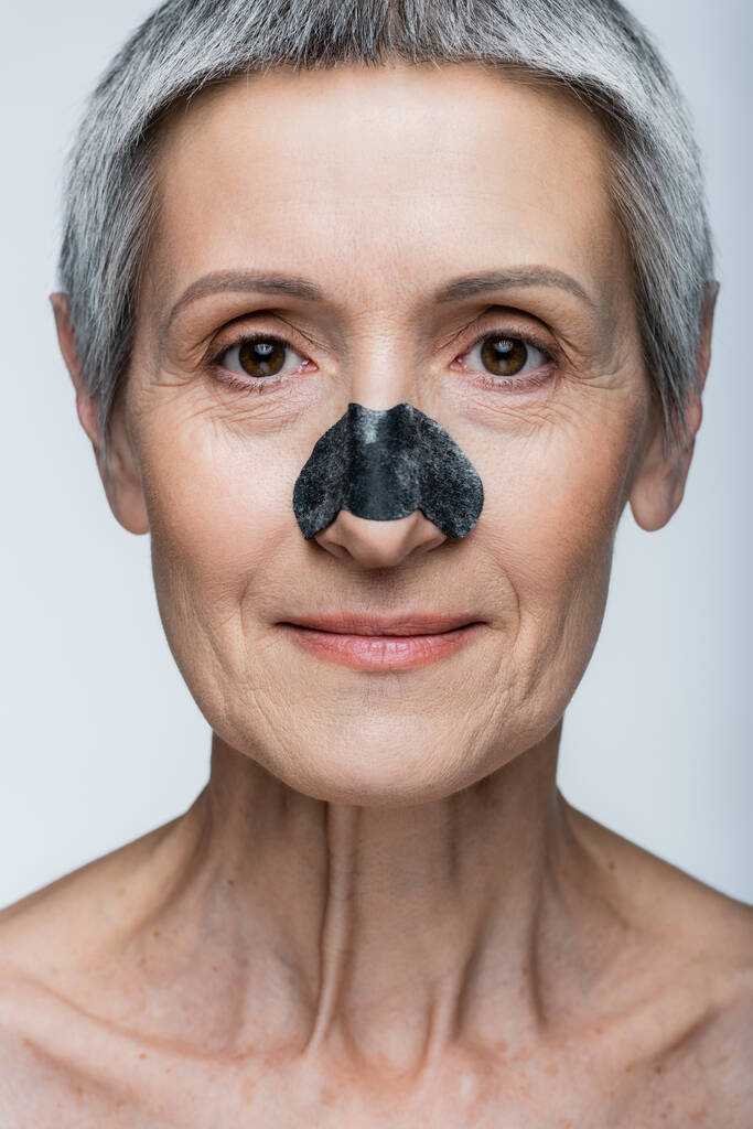gros plan de la femme d'âge moyen souriante avec les cheveux gris et patch sur le nez isolé sur gris  - Photo, image