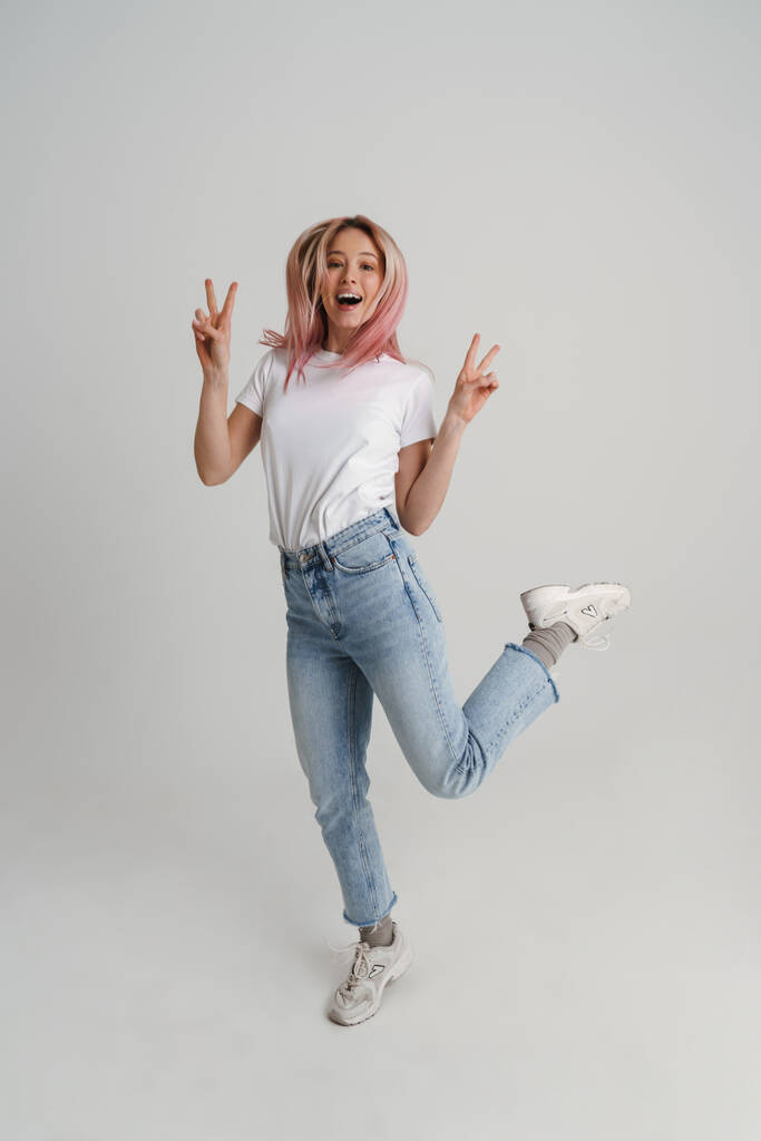 Happy young woman in casual wear jumping over gray wall background, full length portrait - Photo, Image