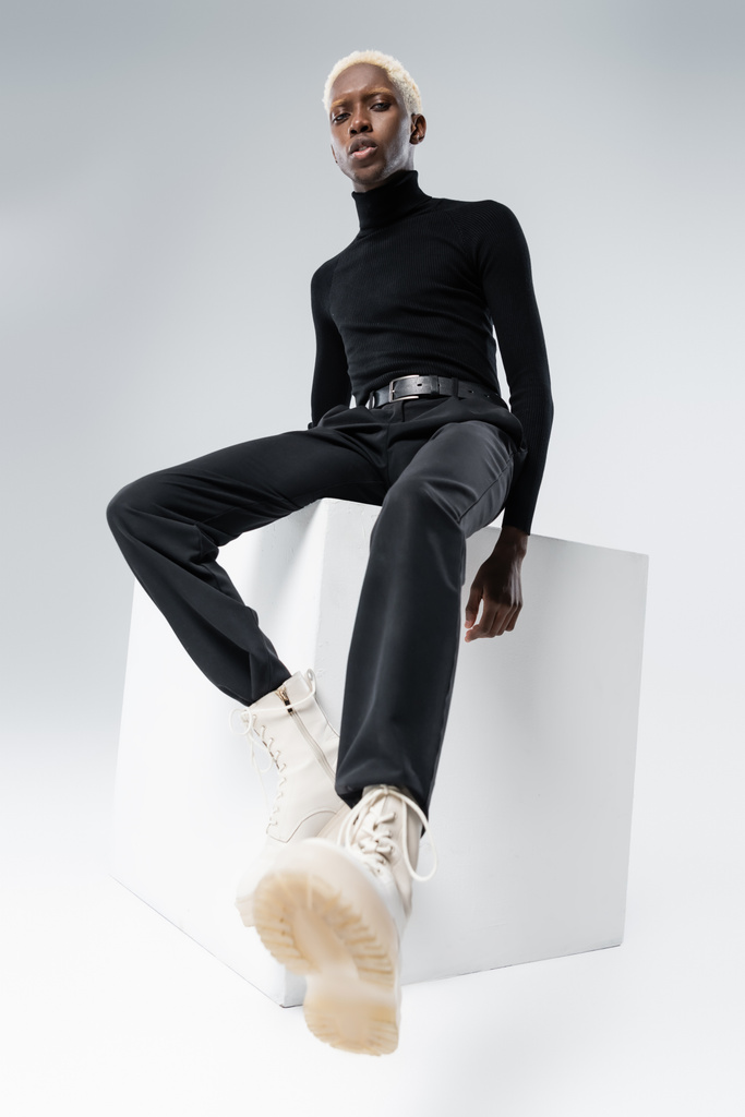 alacsony szög kilátás fiatal afro-amerikai férfi elegáns ruhát ül kockán szürke  - Fotó, kép