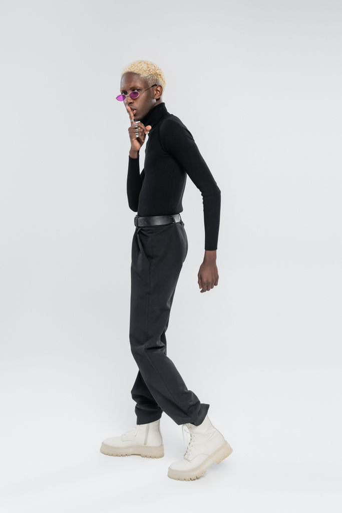 teljes hossza szőke afro-amerikai férfi garbó és rózsaszín napszemüveg mutatja csend jel szürke - Fotó, kép