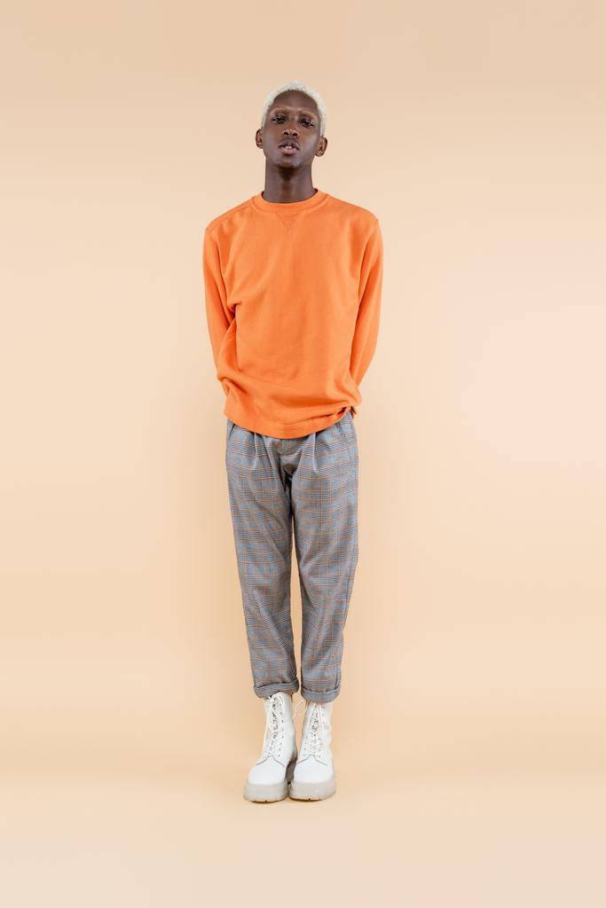 comprimento total de loira homem americano africano em camisola laranja posando no bege - Foto, Imagem