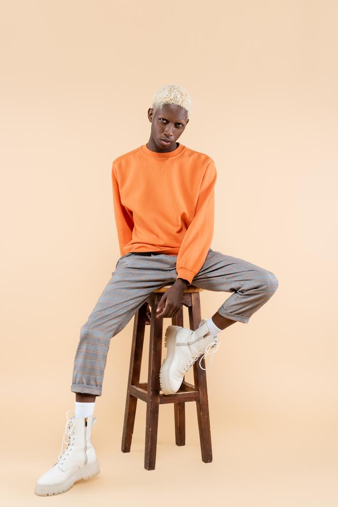 повна довжина молодого афроамериканця в светрі, сидячи на стільці на бежевому
 - Фото, зображення
