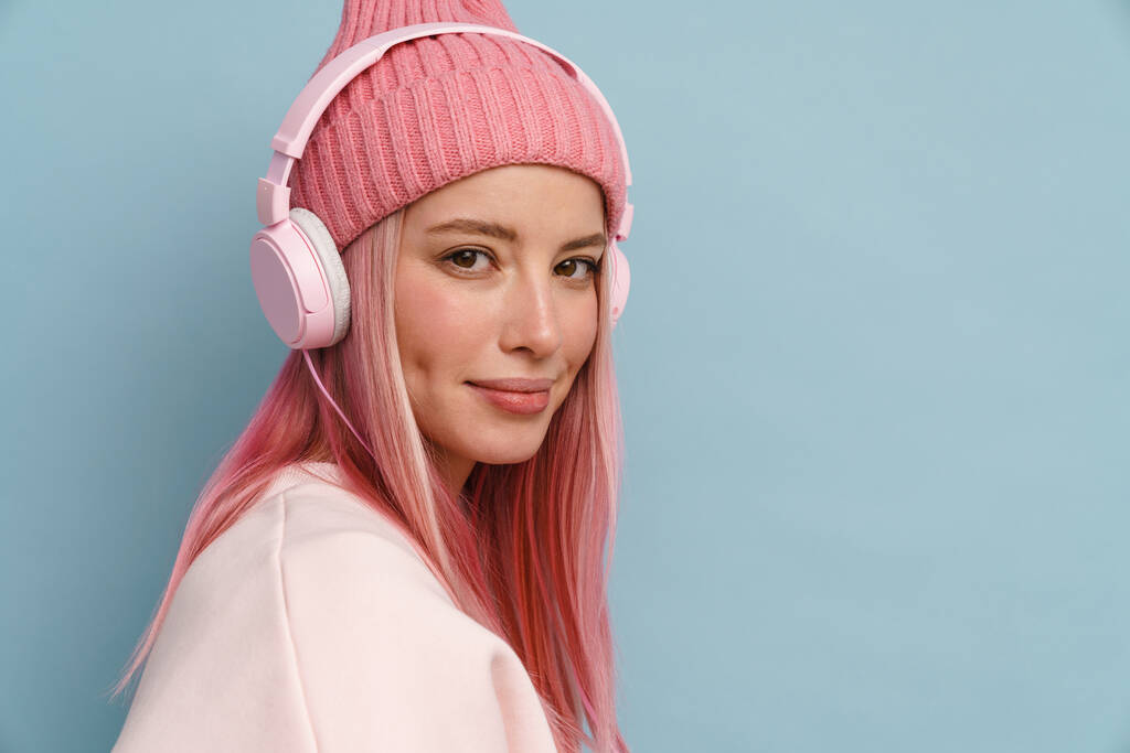 Young white woman wearing pink hat listening music with headphones isolated over blue wall - Photo, Image