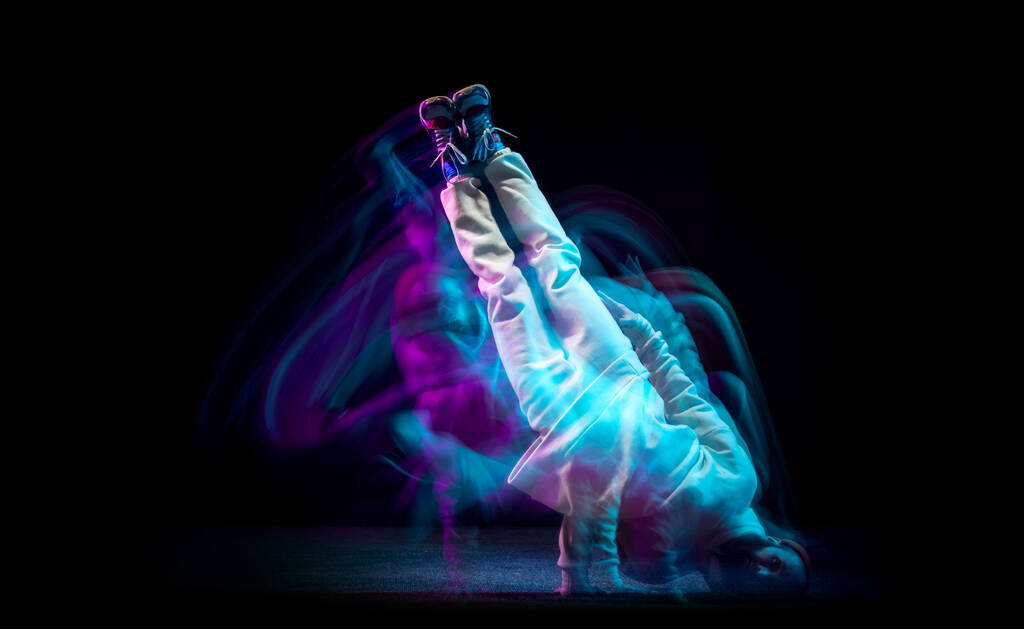 Levez la main. Une énergie jeune homme sportif flexible dansant hip-hop ou breakdance en tenue blanche sur fond sombre dans une lumière au néon bleu mélangé. Sport, art, action, mouvements - Photo, image