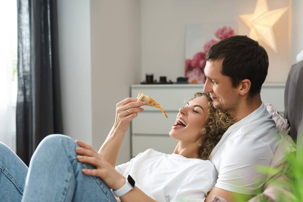 Couple paresseux et heureux relaxant à la maison. Manger de la pizza et se coucher sur le lit. - Photo, image