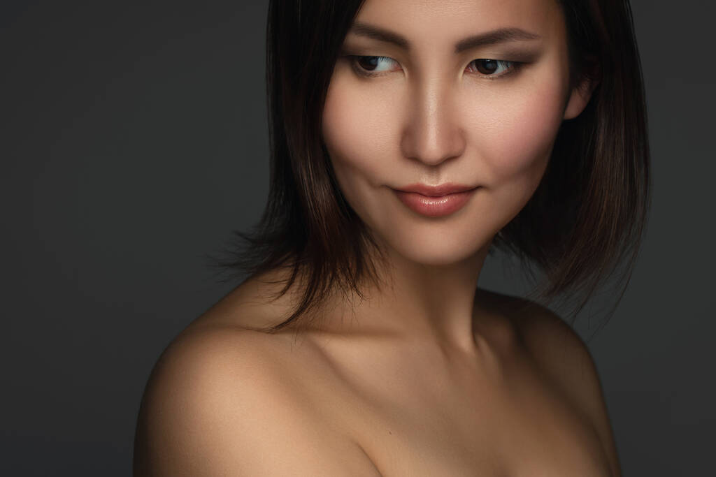 Nuoren ja kauniin aasialaisen naisen muotokuva, jolla on lyhyet tummat hiukset harmaalla taustalla - Valokuva, kuva