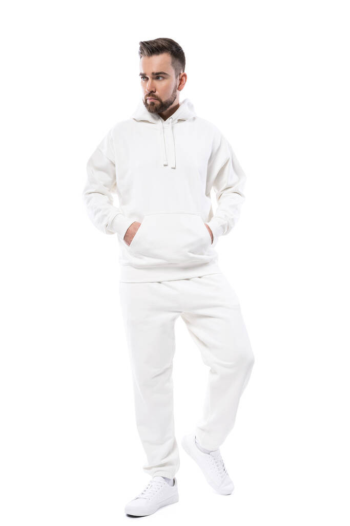 Schöner Mann mit weißem Kapuzenpulli und weißer Hose auf weißem Hintergrund - Foto, Bild
