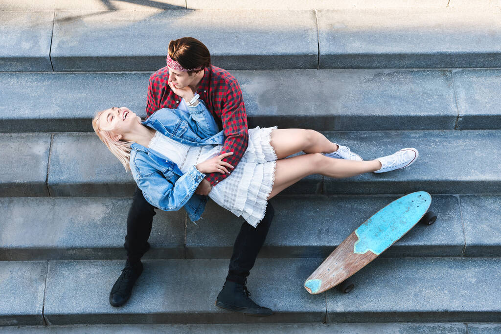 Horní pohled na stylový teenagerský pár s longboardem sedí na betonových schodech - Fotografie, Obrázek