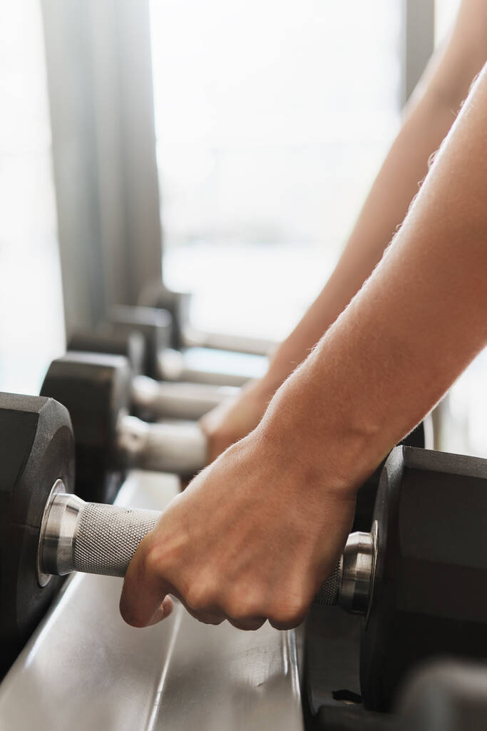 Closeup of female hands and dumbbells on the rack in gym - Photo, Image