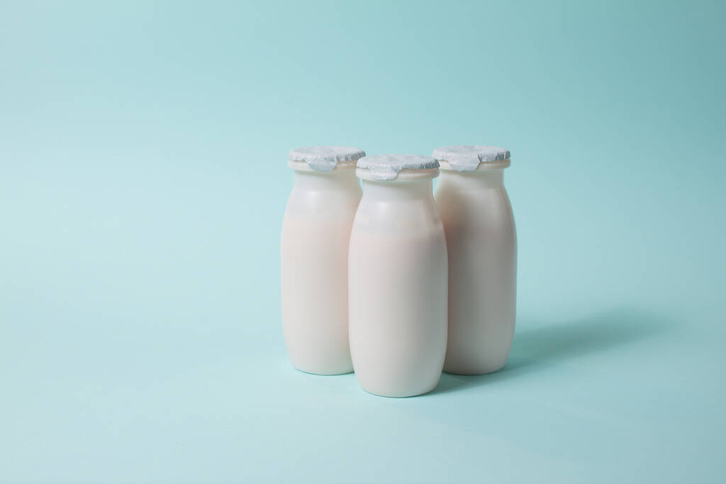 Botellas con probióticos y prebióticos bebida láctea sobre fondo azul claro. Yogur bio con microorganismos útiles. Producción con aditivos biológicamente activos. Fermentación y dieta alimentos saludables. - Foto, imagen