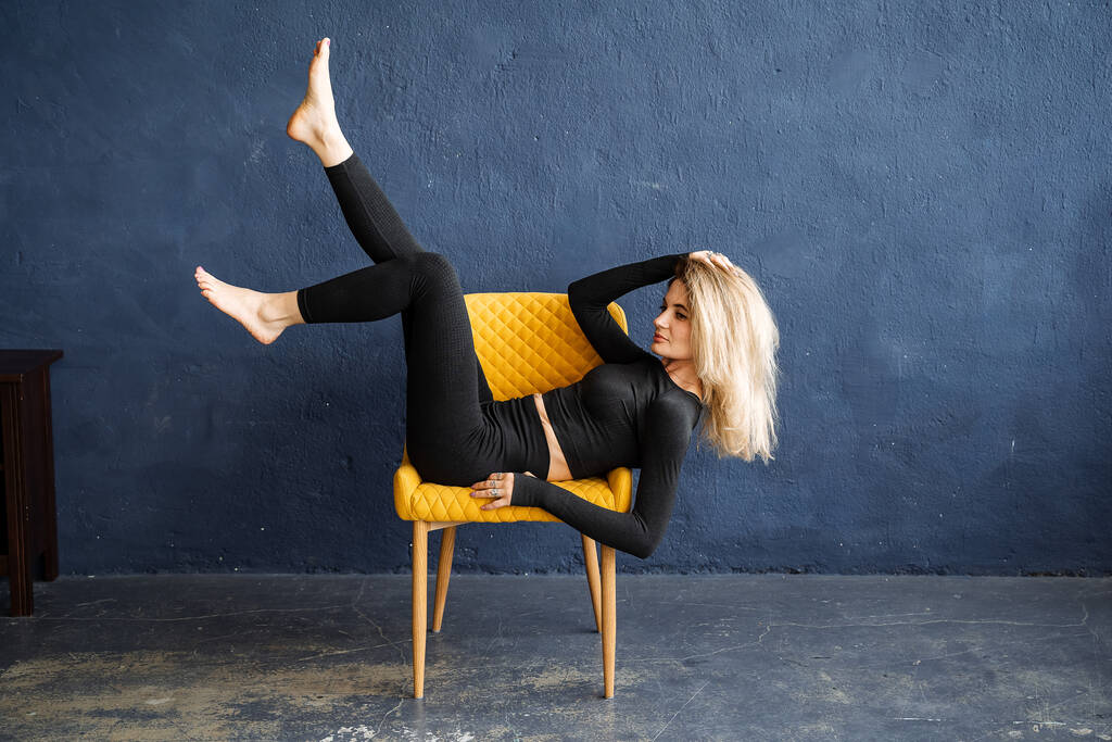Une fille blonde élégante repose de façon impressionnante sur une chaise. Style de yoga. poses inhabituelles pour les portraits. Bon étirement et grâce. Photo de haute qualité - Photo, image