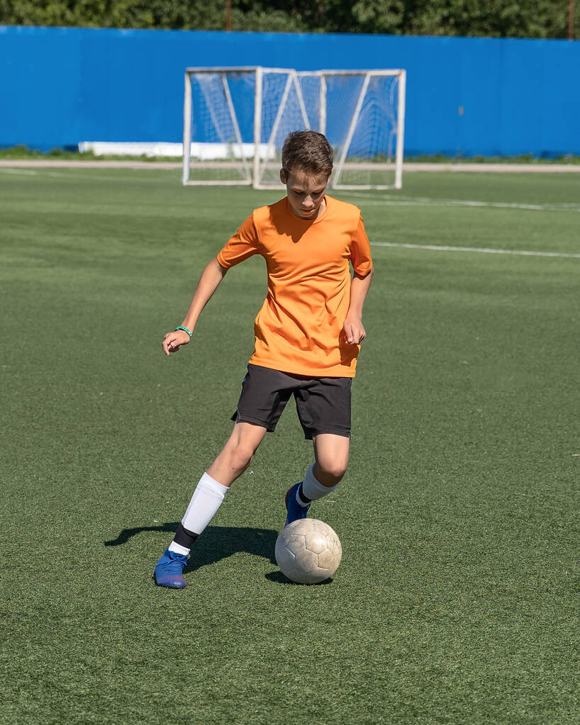 Al niño le encanta jugar al fútbol, entrena con la pelota en el césped artificial y marca un gol, el niño juega fútbol. - Foto, imagen