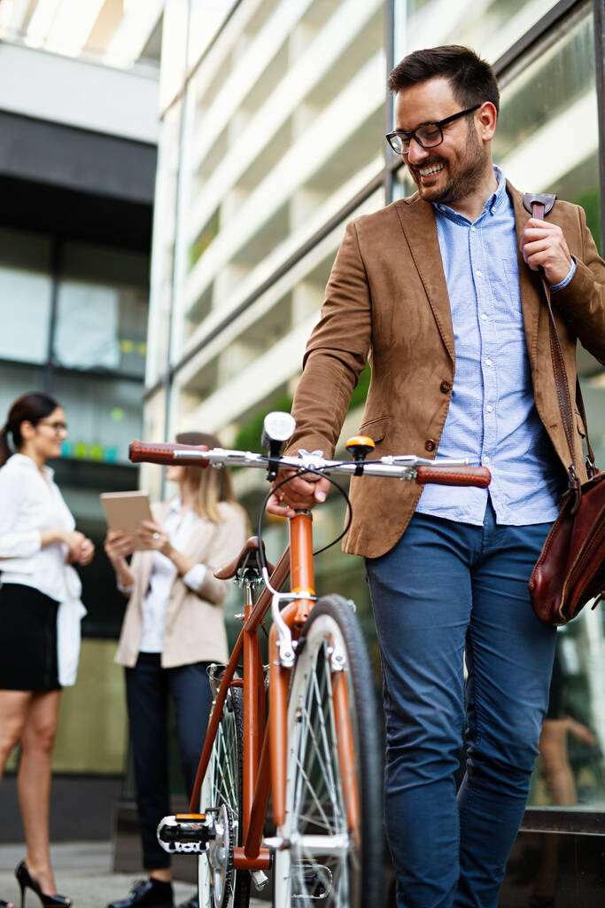 Portrait of happy fit young business man with bicycle in modern city outdoors. - Photo, Image