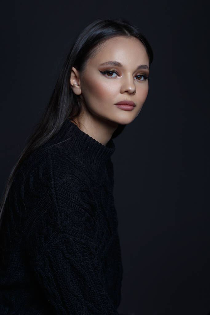 Stylish portrait of a beautiful brunette girl in a black sweater isolated on a black background. - Photo, Image
