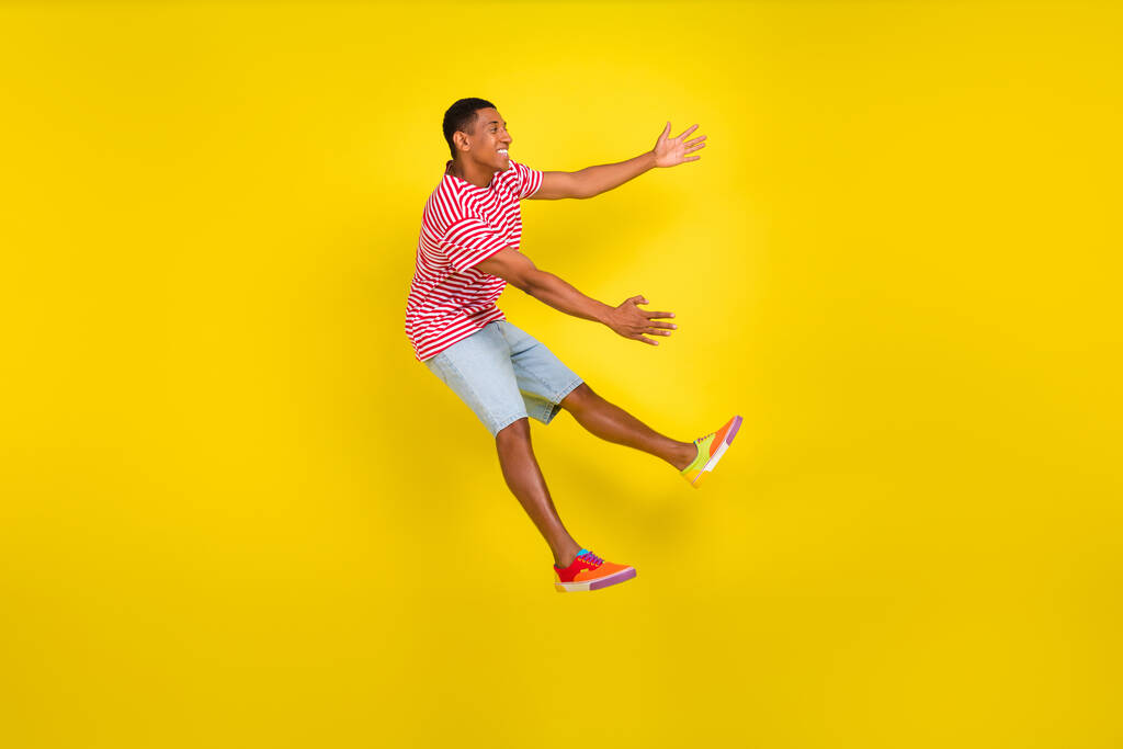 Volledige lengte profiel zijkant foto van jongen springen knuffel grote advertentie dragen rood gestreepte kleren geïsoleerd over gele kleur achtergrond - Foto, afbeelding