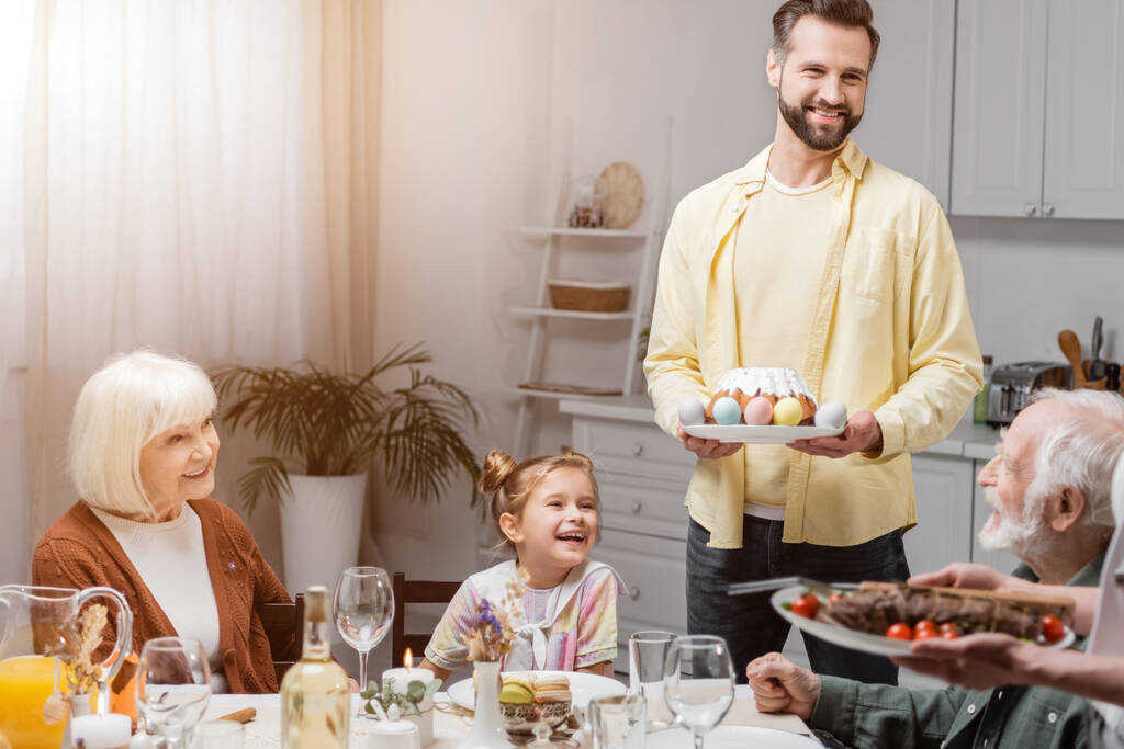 homme heureux avec gâteau de Pâques et oeufs peints pendant le dîner de Pâques en famille - Photo, image