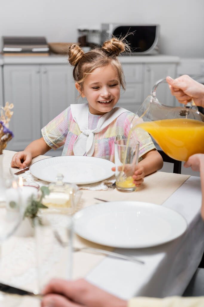 tiener meisje glimlachen in de buurt moeder gieten sinaasappelsap tijdens Pasen diner - Foto, afbeelding