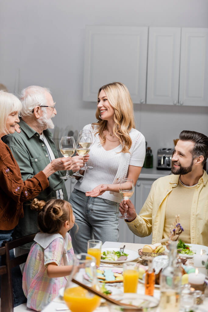 キッチンでのイースターディナーの間にワイングラスをクリックする陽気な家族 - 写真・画像