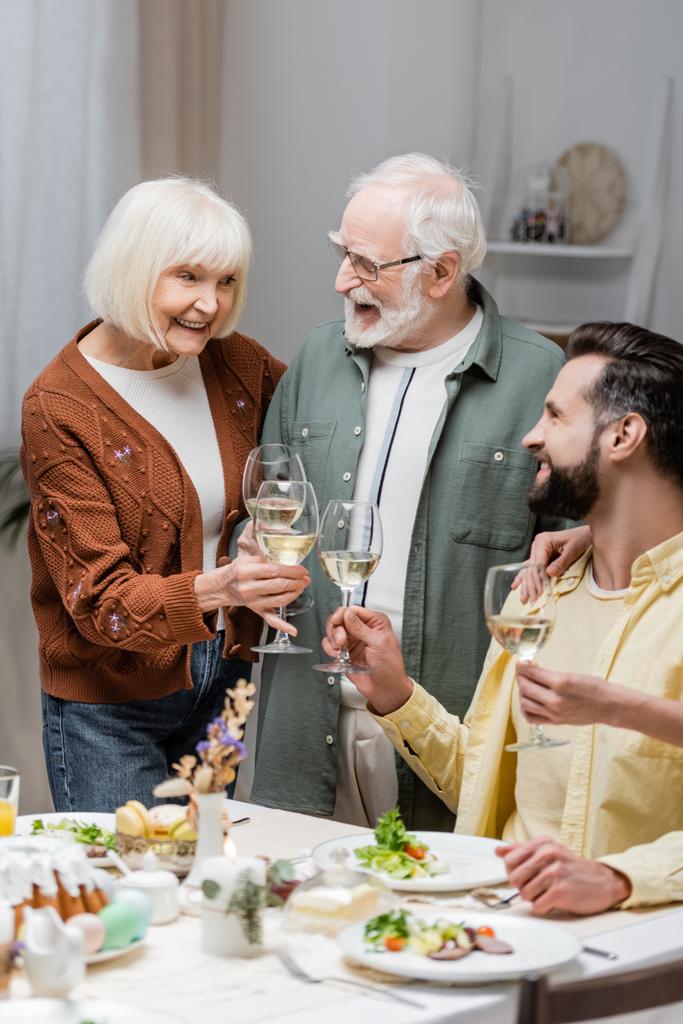 happy senior couple clinking wine glasses with adult son during easter dinner - Photo, Image
