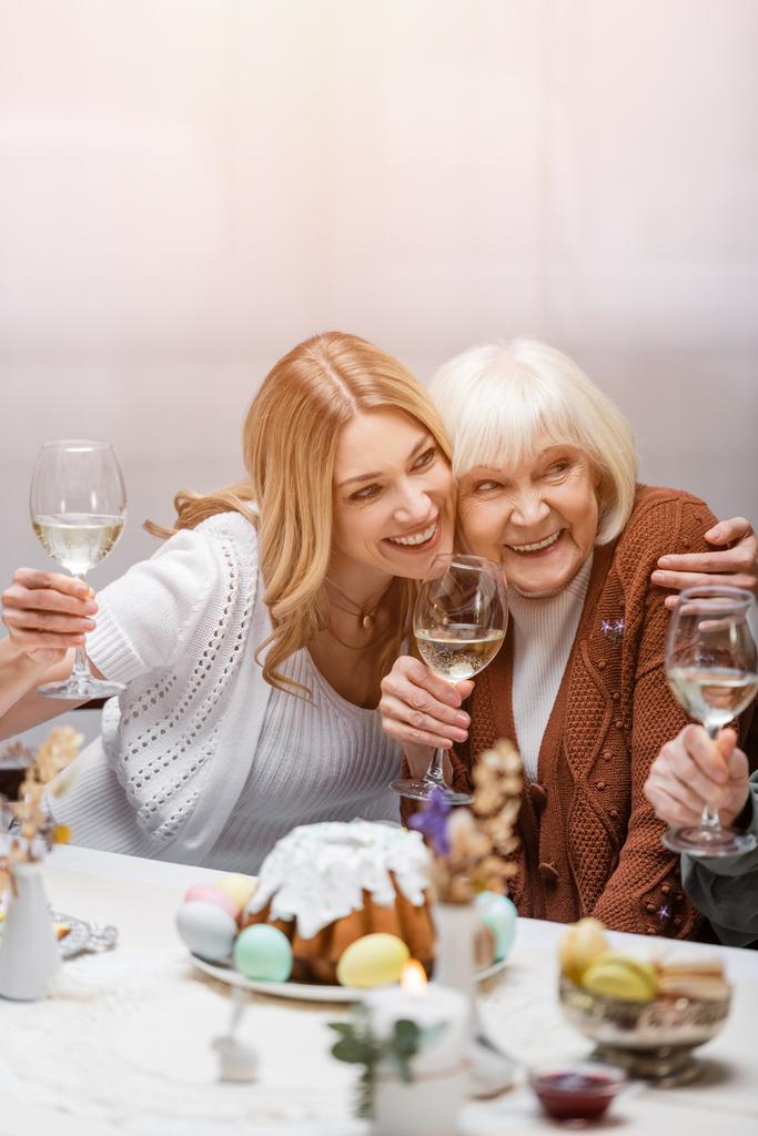 ευτυχισμένη μητέρα και κόρη με ποτήρια κρασιού αγκαλιάζει κατά τη διάρκεια του δείπνου Πάσχα - Φωτογραφία, εικόνα