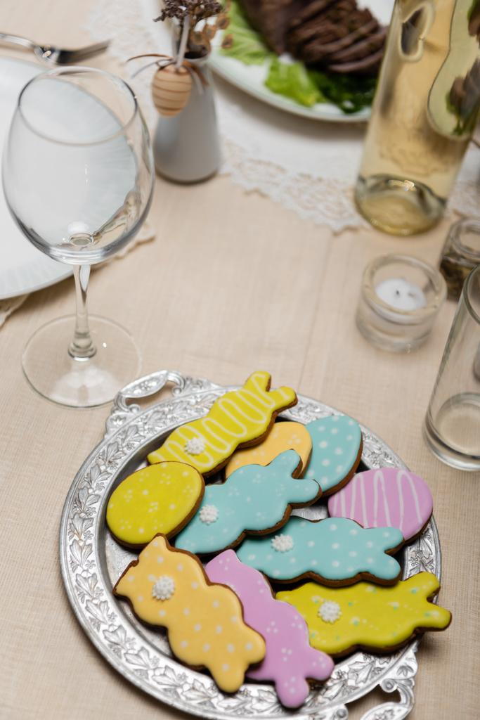 vista de alto ângulo de cookies coloridos perto de garrafa de vinho na mesa servida para o jantar de Páscoa - Foto, Imagem