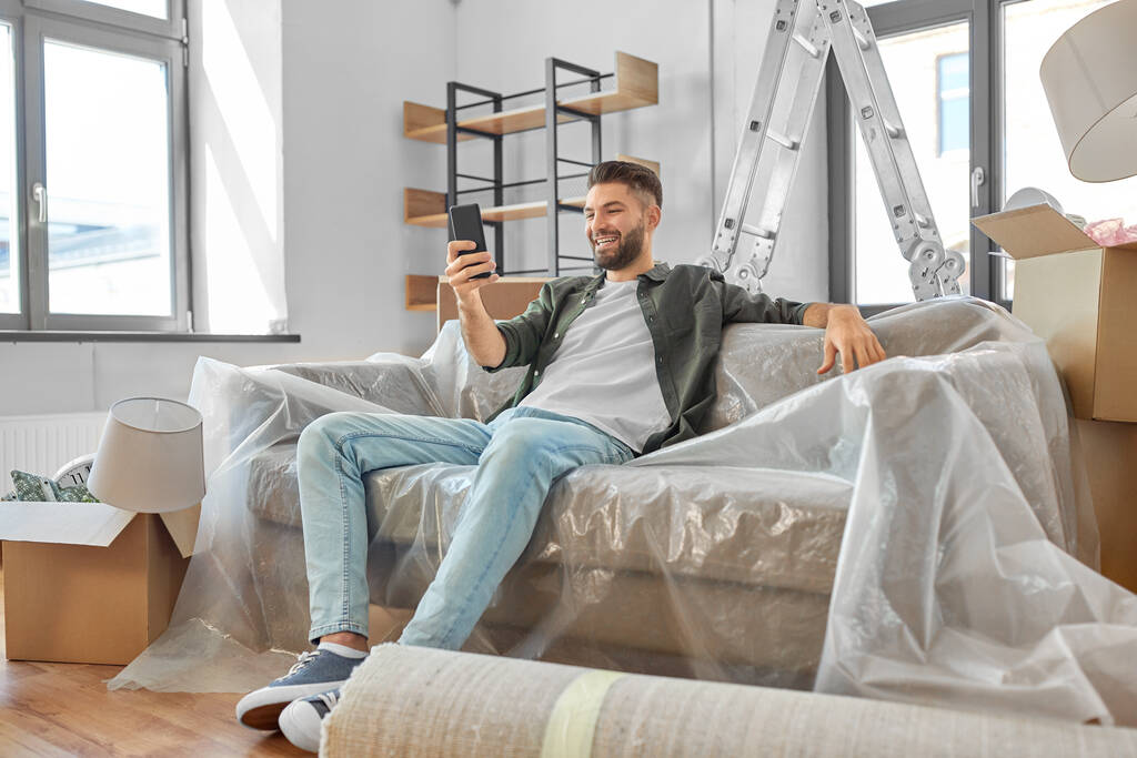 smiling man with smartphone moving into new home - Photo, Image