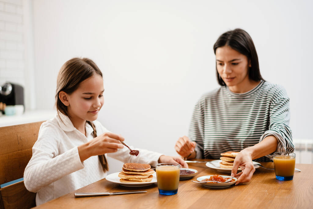 Wesoła piękna matka i córka uśmiechnięte podczas śniadania w przytulnej kuchni - Zdjęcie, obraz