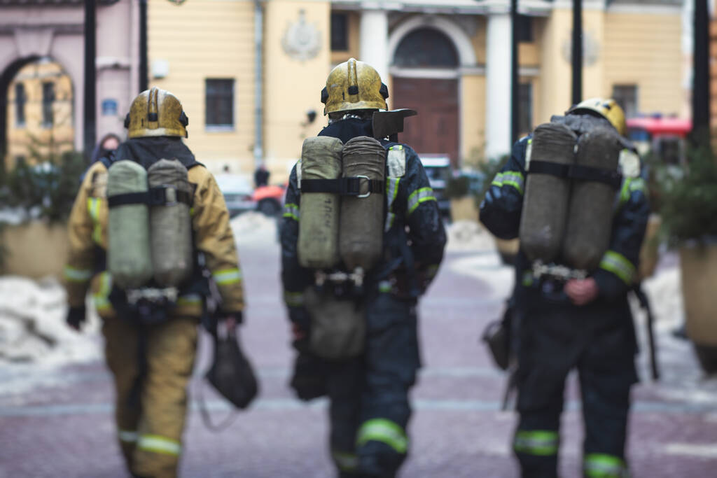 Gruppo di vigili del fuoco in uniforme durante le operazioni antincendio nelle strade della città, vigili del fuoco con il veicolo antincendio sullo sfondo, emergenza  - Foto, immagini