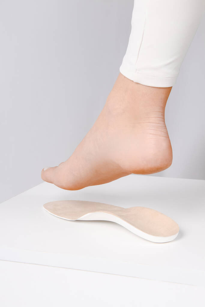 Wkładki medyczne. Izolowane wkładki ortopedyczne na białym tle. Leczenie i profilaktyka chorób płaskich stóp i stóp. Pielęgnacja stóp. Warstwy przecięcia podeszwy. Noga zwisająca nad wkładką - Zdjęcie, obraz