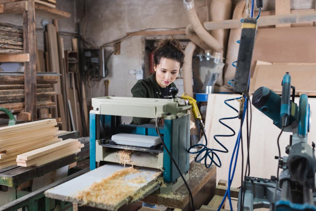 Charpentier travaillant sur raboteuse d'épaisseur près de sciure de bois en atelier  - Photo, image