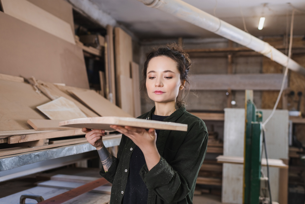 Joven carpintero sosteniendo tablero de madera borrosa en taller  - Foto, imagen